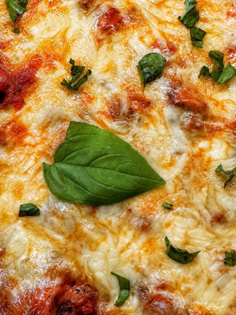Close-up of baked ziti with browned bubbly mozzarella and fresh basil on top