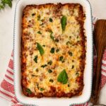 Easy cheesy baked ziti in a white baking dish, topped with melted golden mozzarella and fresh basil leaves