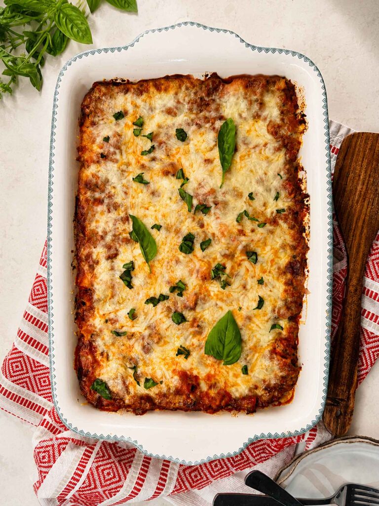 Easy cheesy baked ziti in a white baking dish, topped with melted golden mozzarella and fresh basil leaves