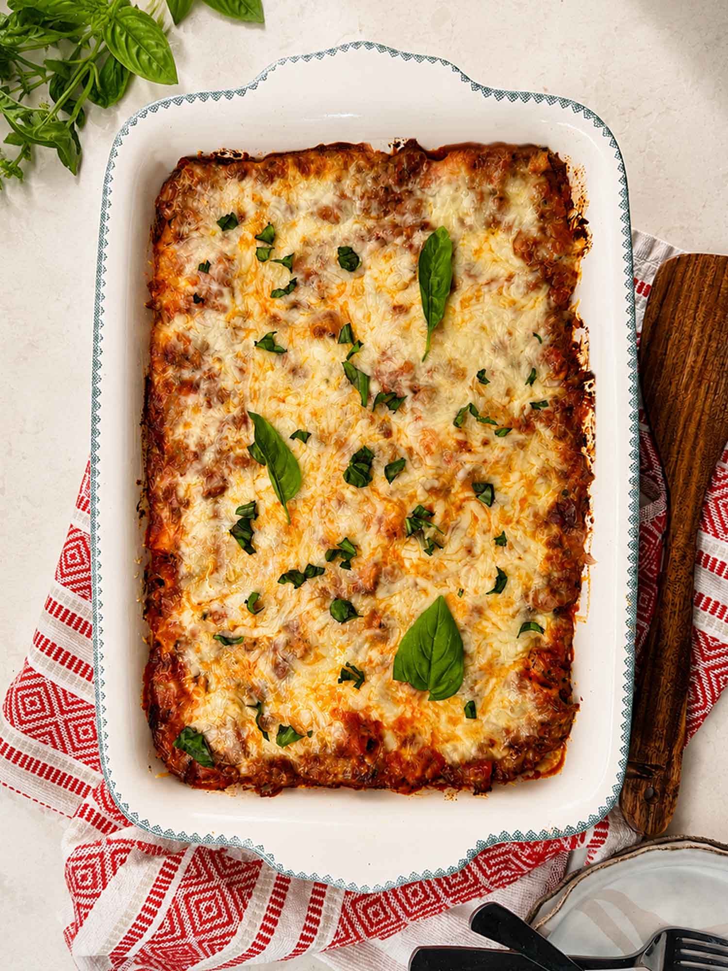 Easy cheesy baked ziti in a white baking dish, topped with melted golden mozzarella and fresh basil leaves