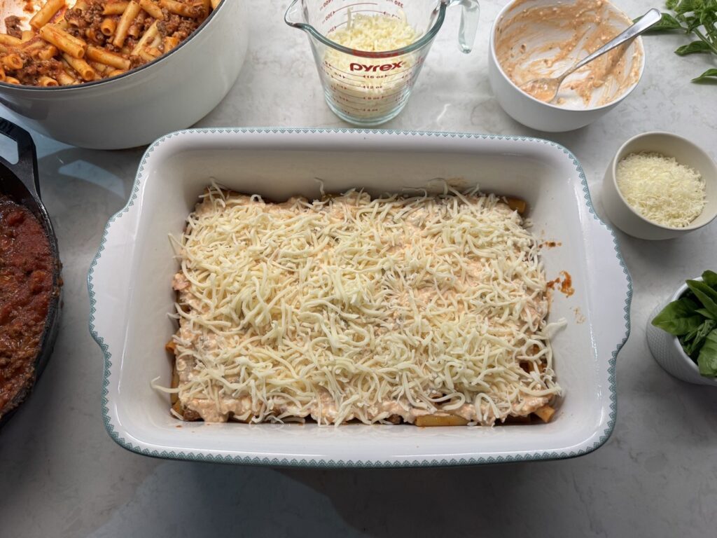 Shredded mozzarella scattered over the ziti in the baking dish