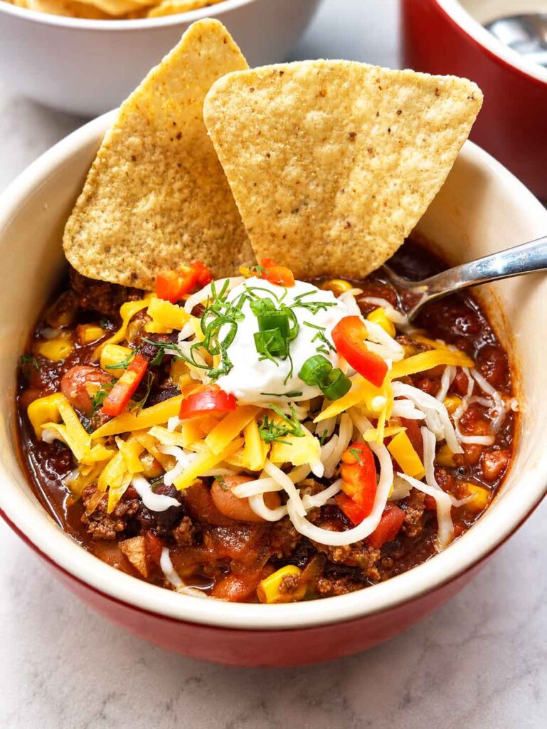 Bowl of taco soup topped with tortilla chips, shredded cheese, sour cream, and red pepper
