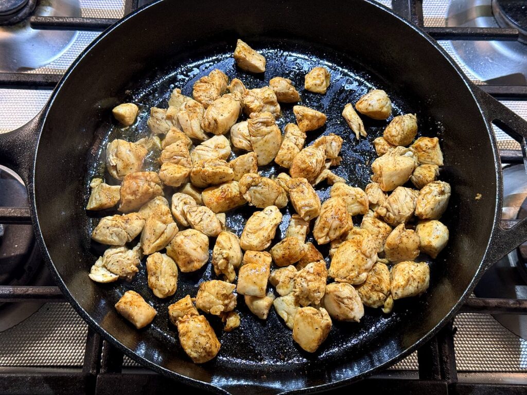 Bite-size pieces of seasoned chicken browning in a cast iron skillet.