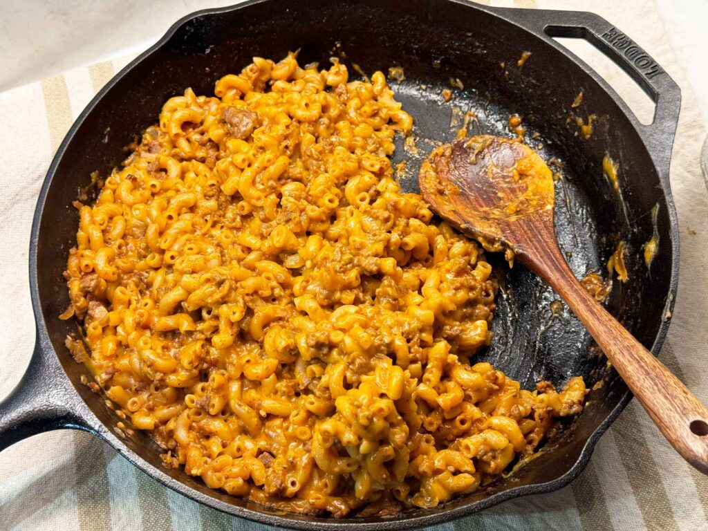 A wooden spoon in a skillet of cheesy homemade hamburger helper