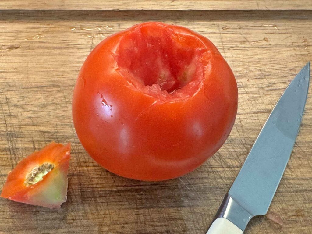 A fresh tomato with the core removed on a cutting board