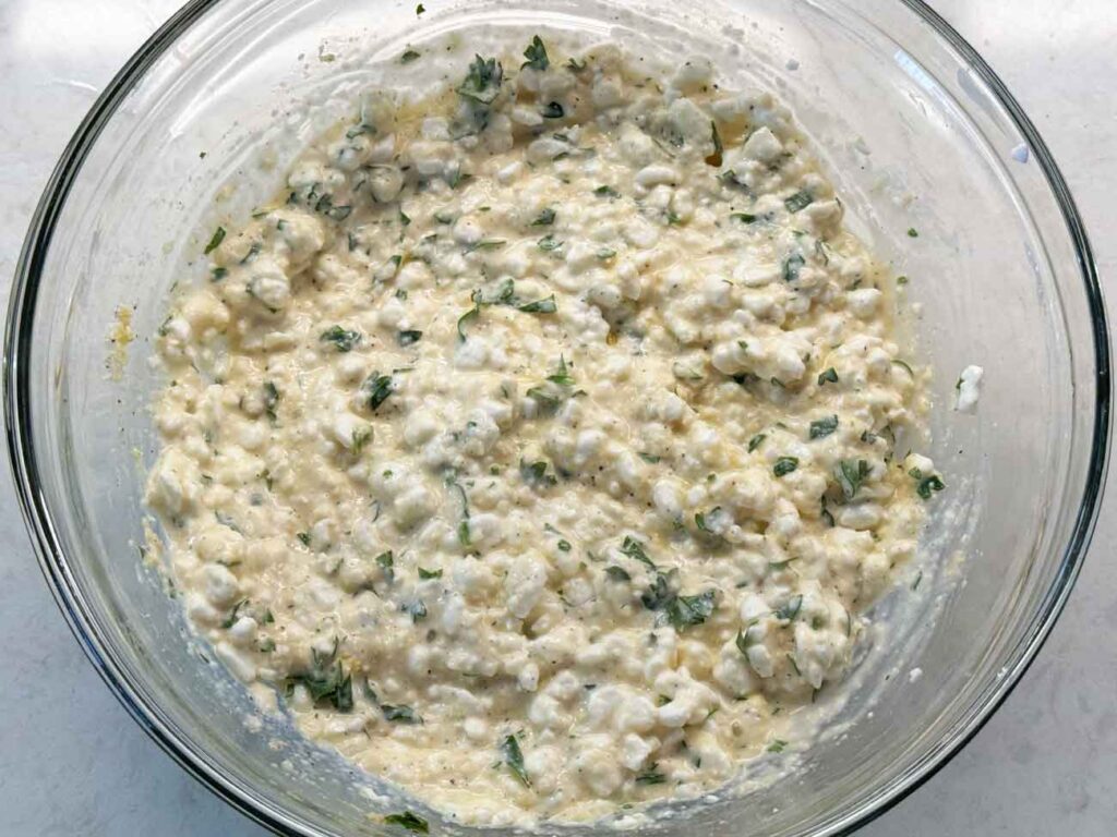 A glass bowl of seasoned cottage cheese filling flecked with parsley.