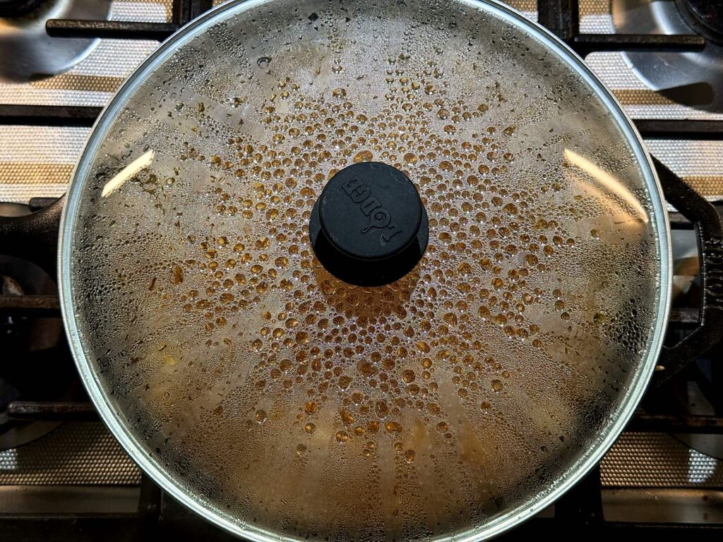 A glass lid covering the skillet as the honey BBQ chicken and rice simmers.