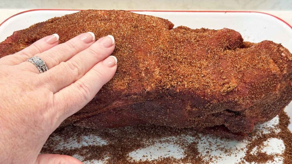Jennifer's hand rubbing the brown sugar spice rub all over a raw pork shoulder