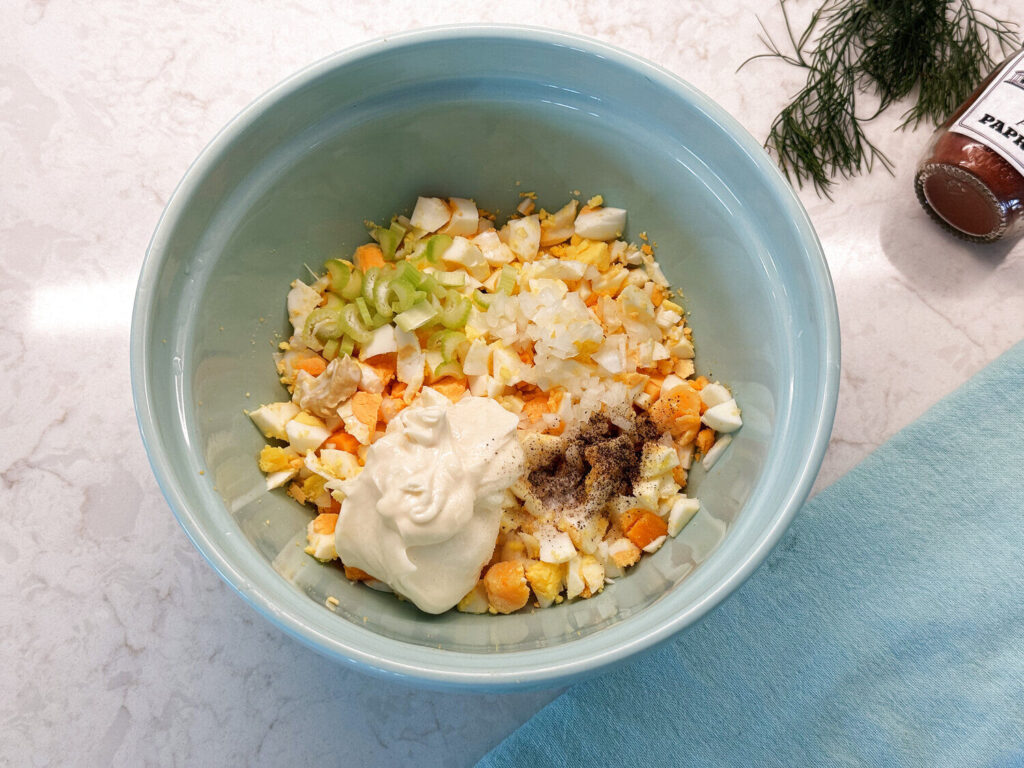 Adding mayonnaise, Dijon, celery, and onion to a bowl of chopped eggs