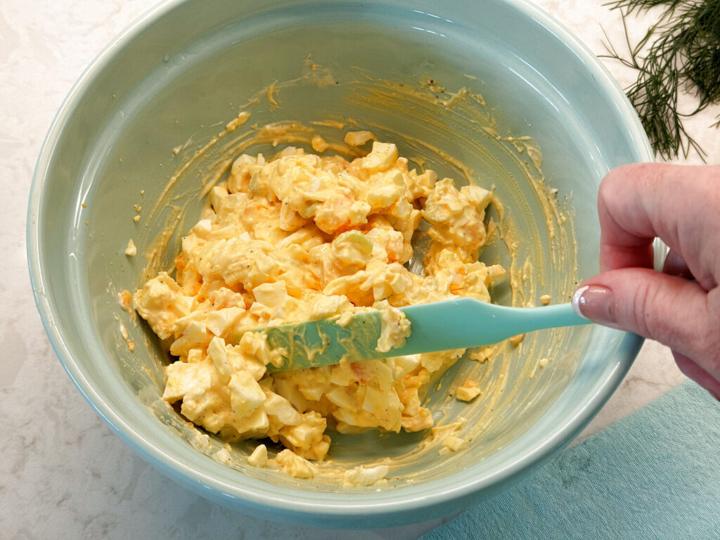 Folding egg salad together with a spatula until creamy
