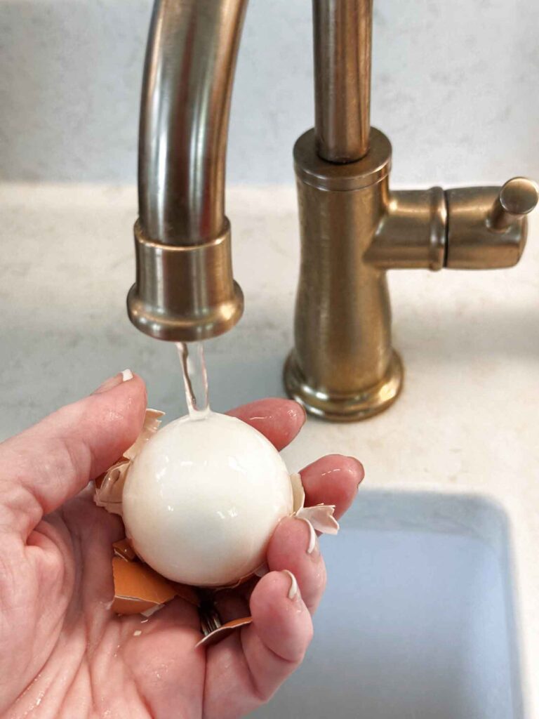 Peeling a hard-boiled egg under a thin stream of running water