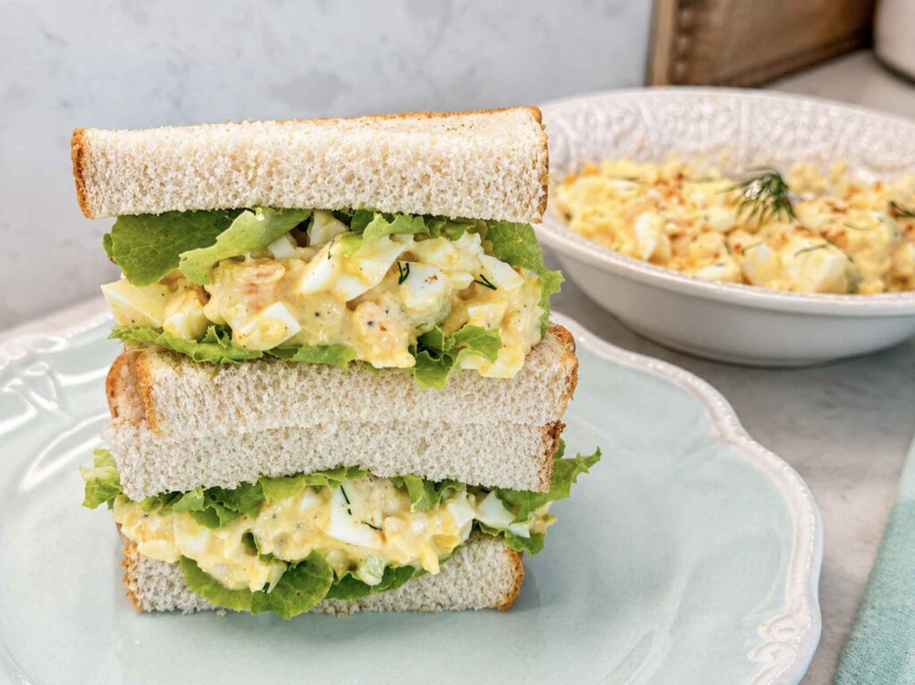 A stacked egg salad sandwich with lettuce on soft white bread