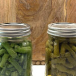 Two finished pint jars of home-canned green beans on a wooden board