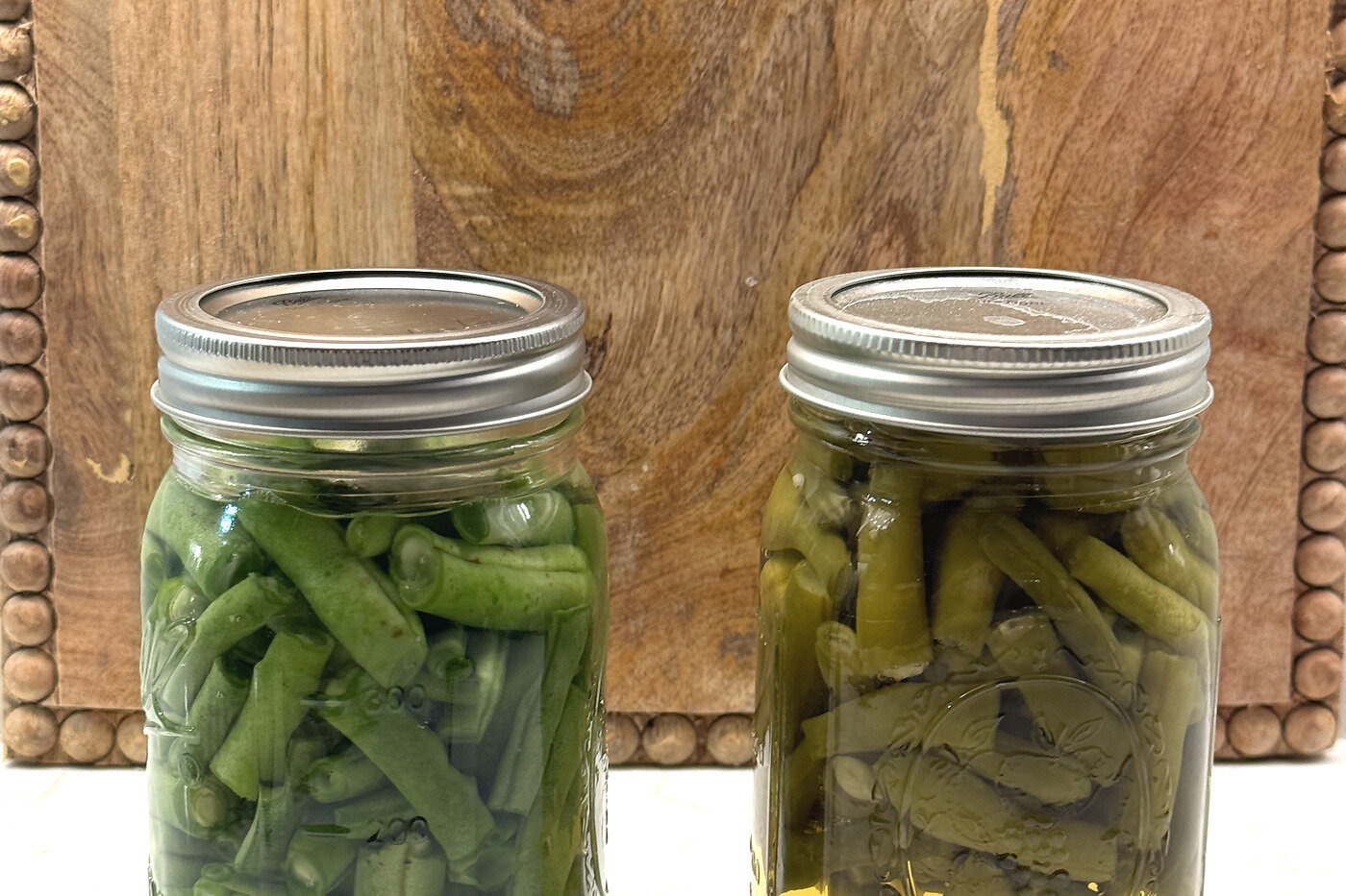 Two finished pint jars of home-canned green beans on a wooden board