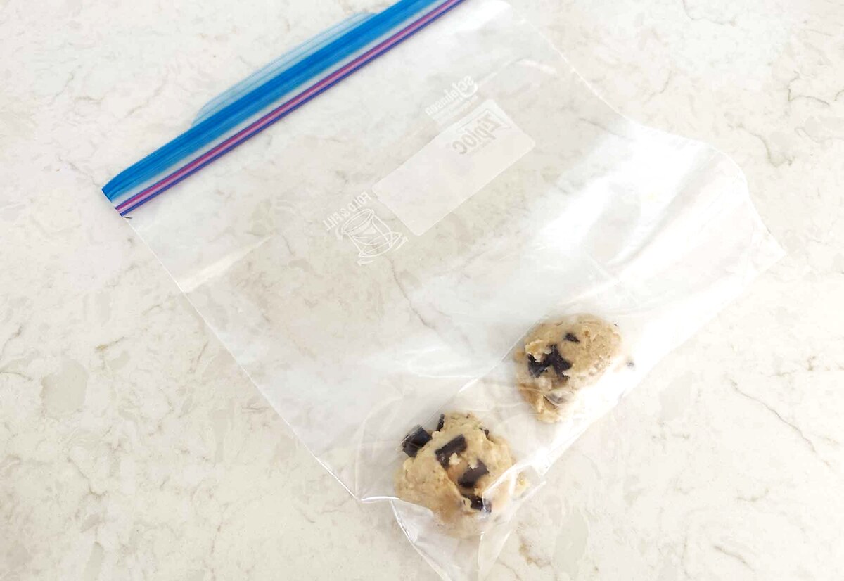 Two frozen sourdough chocolate chip cookie dough balls in a labeled freezer bag.
