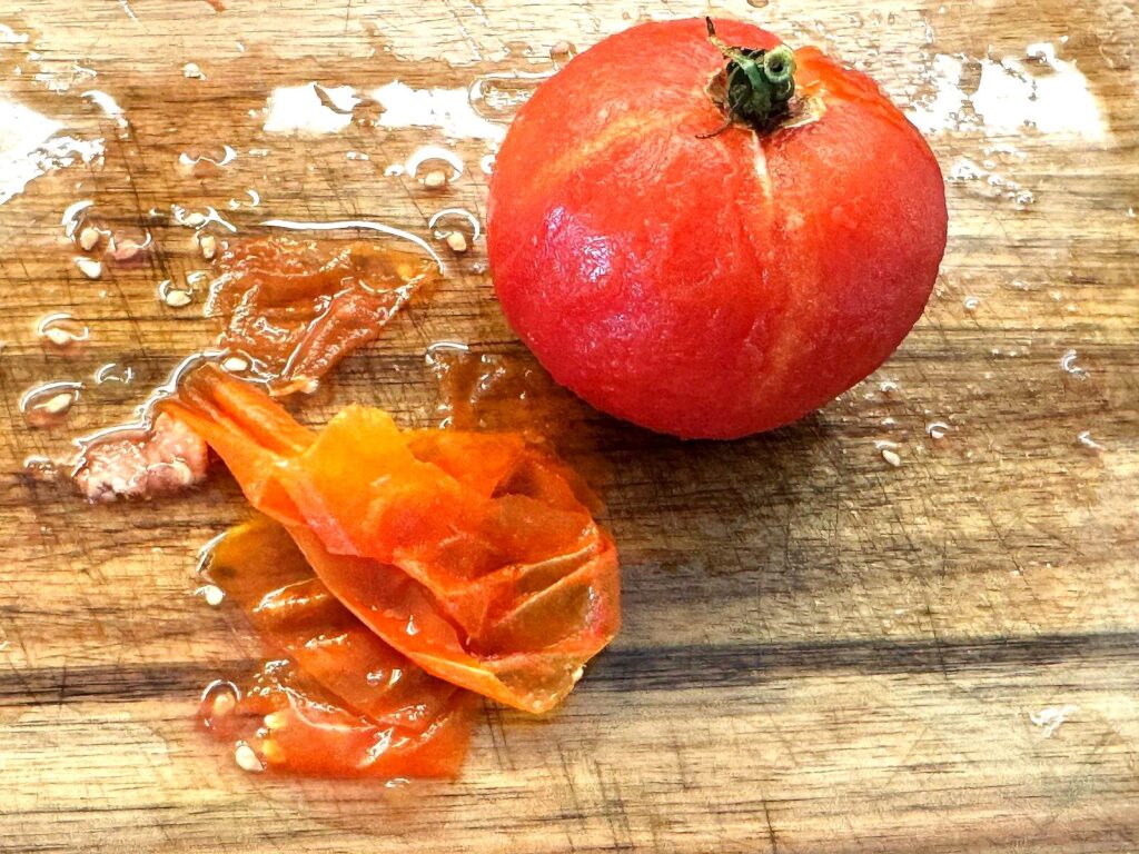 A thawed tomato with its skin slipped off sitting beside it on a cutting board