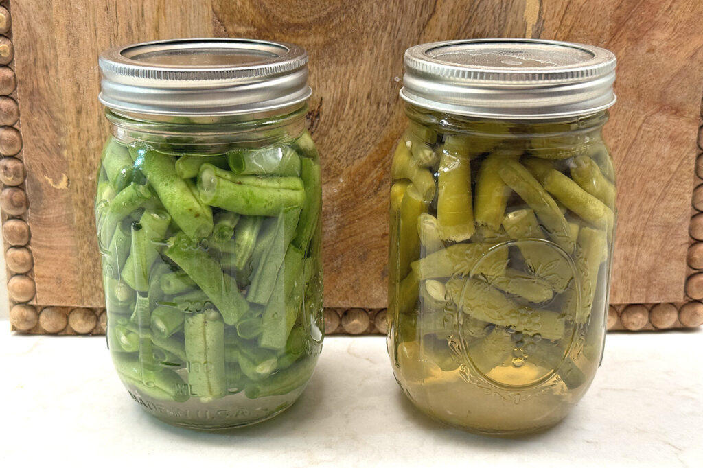 Two pint jars of home-canned green beans on a wooden board