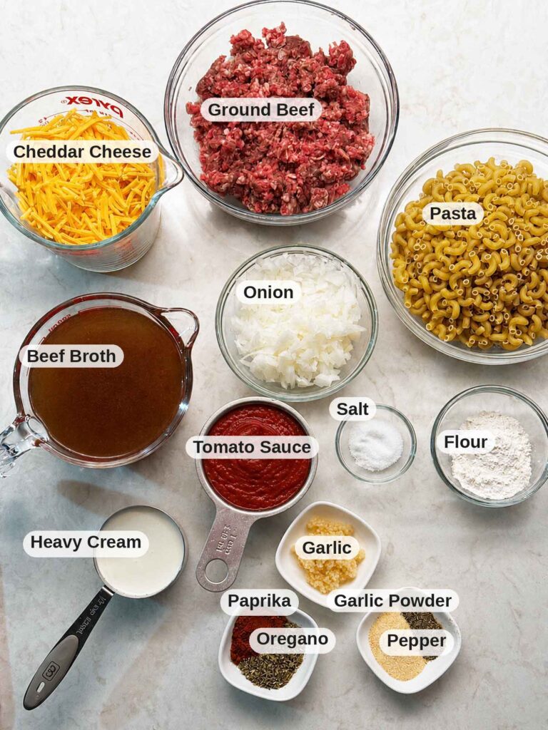 Ingredients to make homemade hamburger helper from scratch, including ground beef, shredded cheddar cheese, and elbow macaroni in bowls
