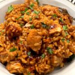 A white bowl of honey BBQ chicken and rice topped with fresh parsley, with a fork resting on the side.