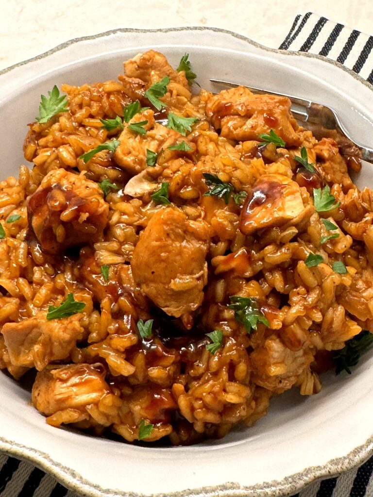 A white bowl of honey BBQ chicken and rice topped with fresh parsley, with a fork resting on the side.