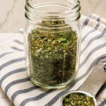 A jar of homemade Italian seasoning with a measuring spoon.