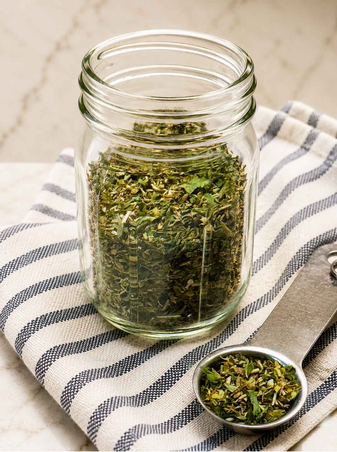 A jar of homemade Italian seasoning with a measuring spoon.