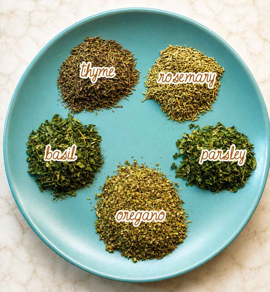 The five herbs for Italian seasoning measured onto a plate and labeled: thyme, rosemary, basil, parsley, and oregano.