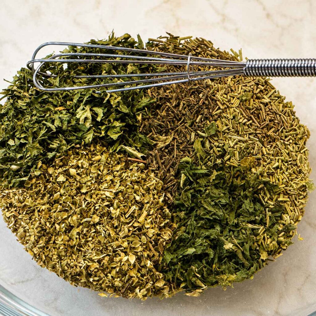 Dried herbs being whisked together in a glass bowl to make homemade Italian seasoning.