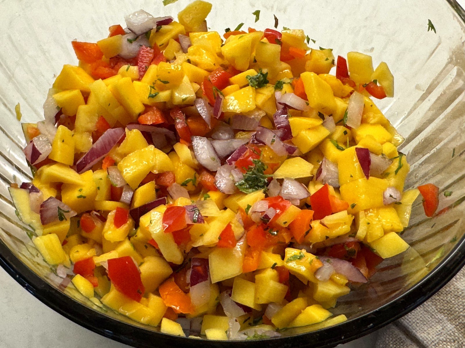 A close-up of finished mango salsa showing bright mango, red bell pepper, red onion, and cilantro
