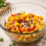 A glass bowl of fresh mango salsa with diced mango, red bell pepper, red onion, and cilantro