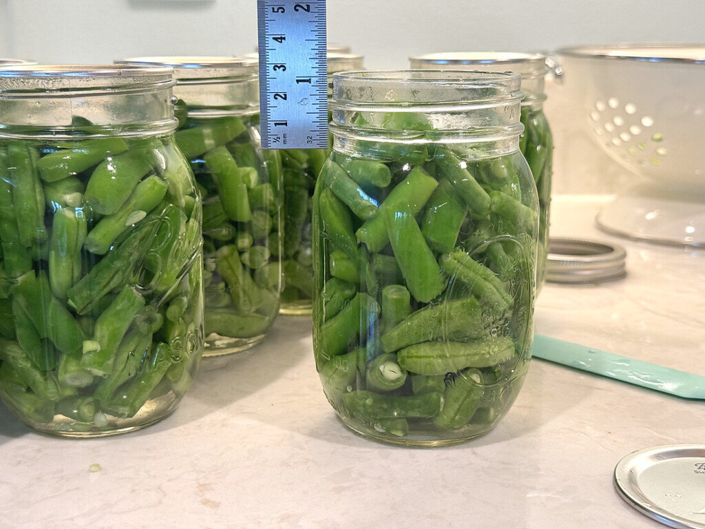 A ruler held against a packed jar to measure exactly one inch of headspace