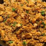 A close-up serving of saucy honey BBQ chicken and rice in a white bowl.