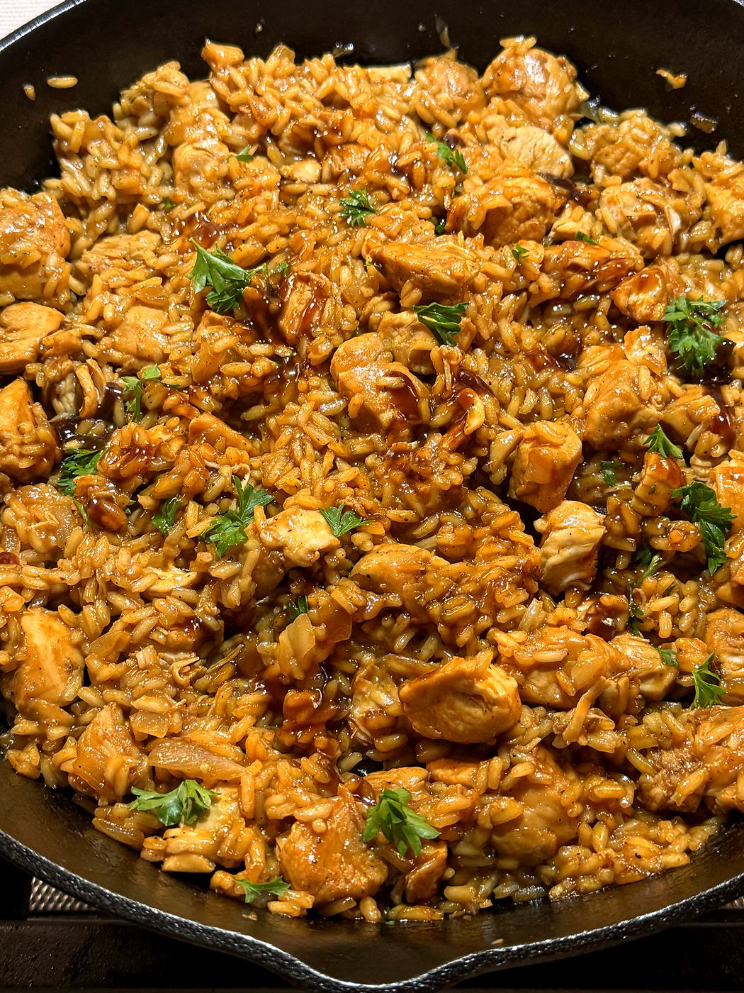 A close-up serving of saucy honey BBQ chicken and rice in a white bowl.