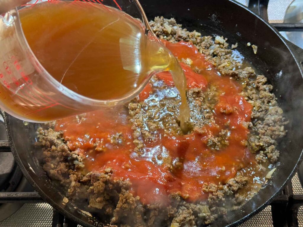 Pouring broth into hamburger helper in skillet