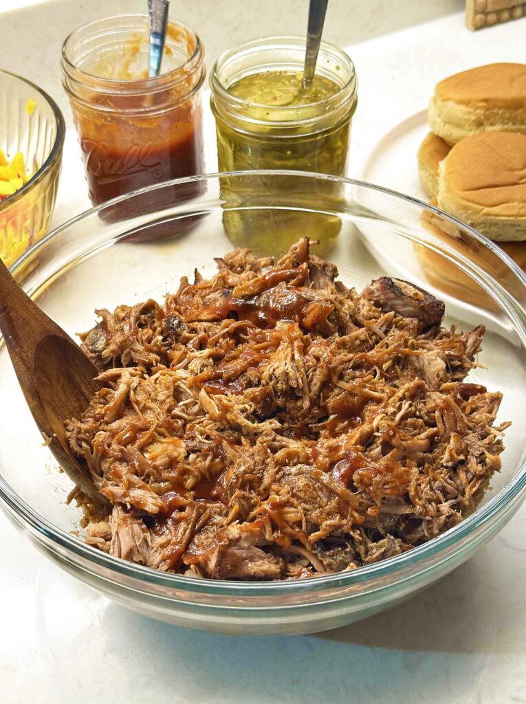 A bowl of shredded pulled pork tossed with BBQ sauce, glossy and moistened with cooking juices