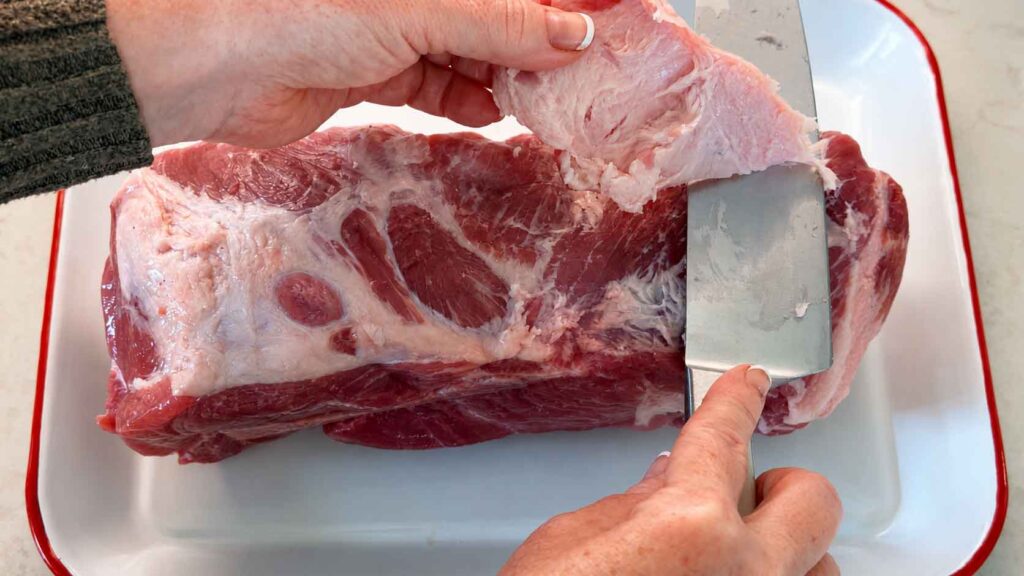 Jennifer trimming the fat cap on a pork shoulder down to about a quarter inch with a sharp knife