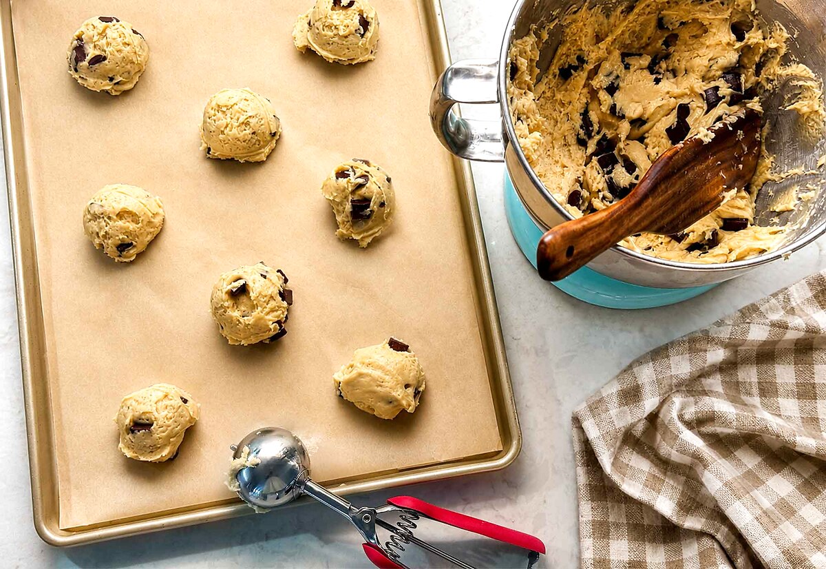 Tall mounds of chilled sourdough chocolate chip cookie dough scooped onto a parchment-lined baking sheet.