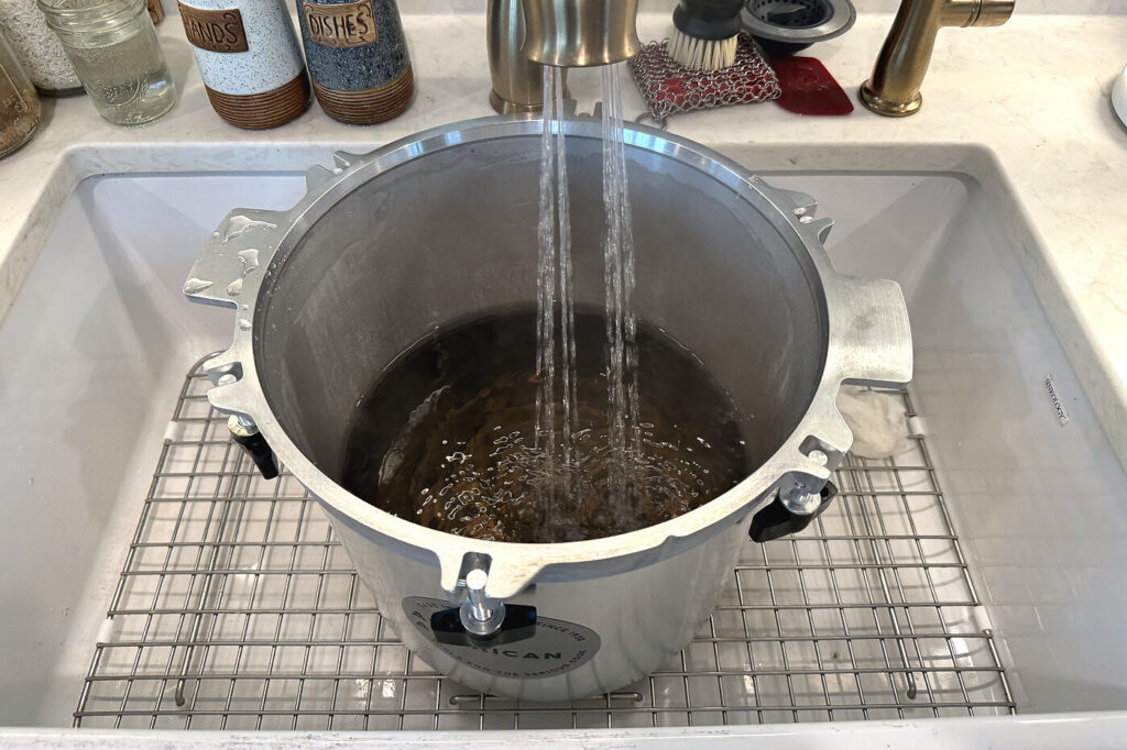 Pressure canner with the rack in the bottom being filled with water in the sink