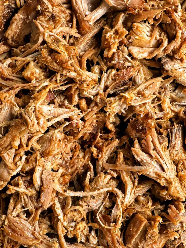 A bowl of shredded pulled pork tossed with BBQ sauce, glossy and moistened with cooking juices