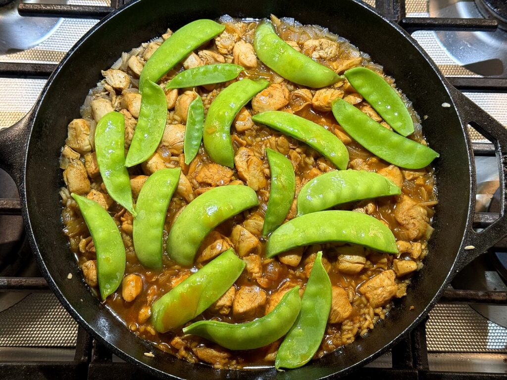 Bright green sugar snap peas scattered over the top of the cooked honey BBQ chicken and rice.