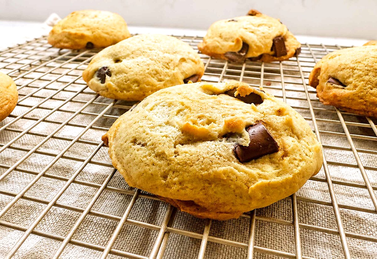 Close-up of a thick, domed sourdough chocolate chip cookie with a melting chocolate chunk, cooling on a wire rack.