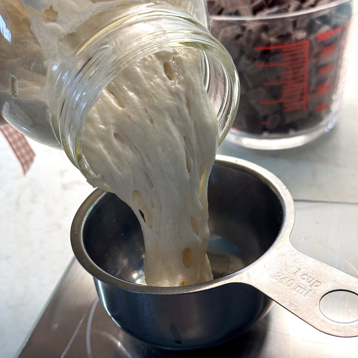 Sourdough discard being poured from a jar into a metal measuring cup.