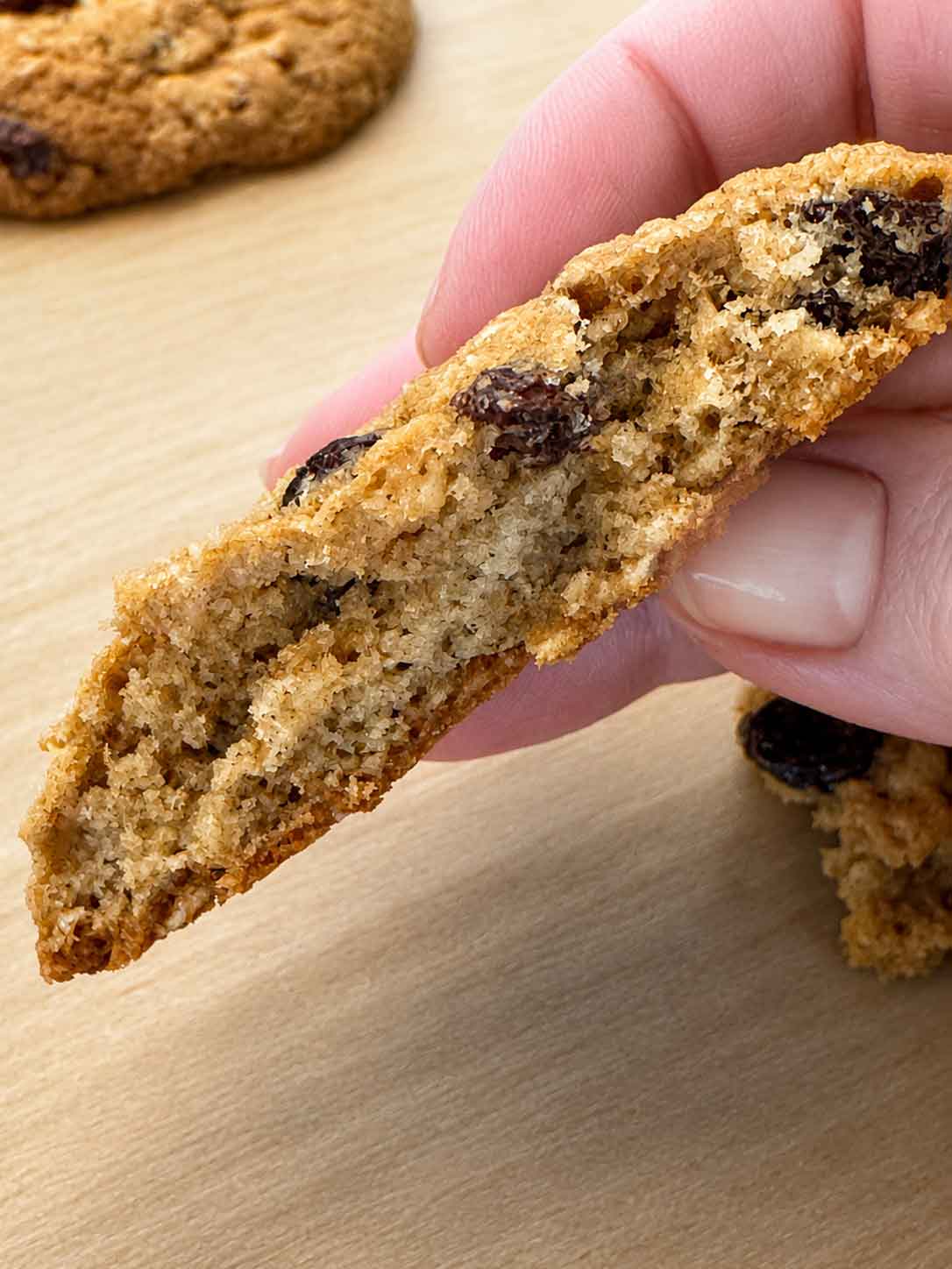A hand holding a sourdough oatmeal cookie broken open to show the soft, chewy center.