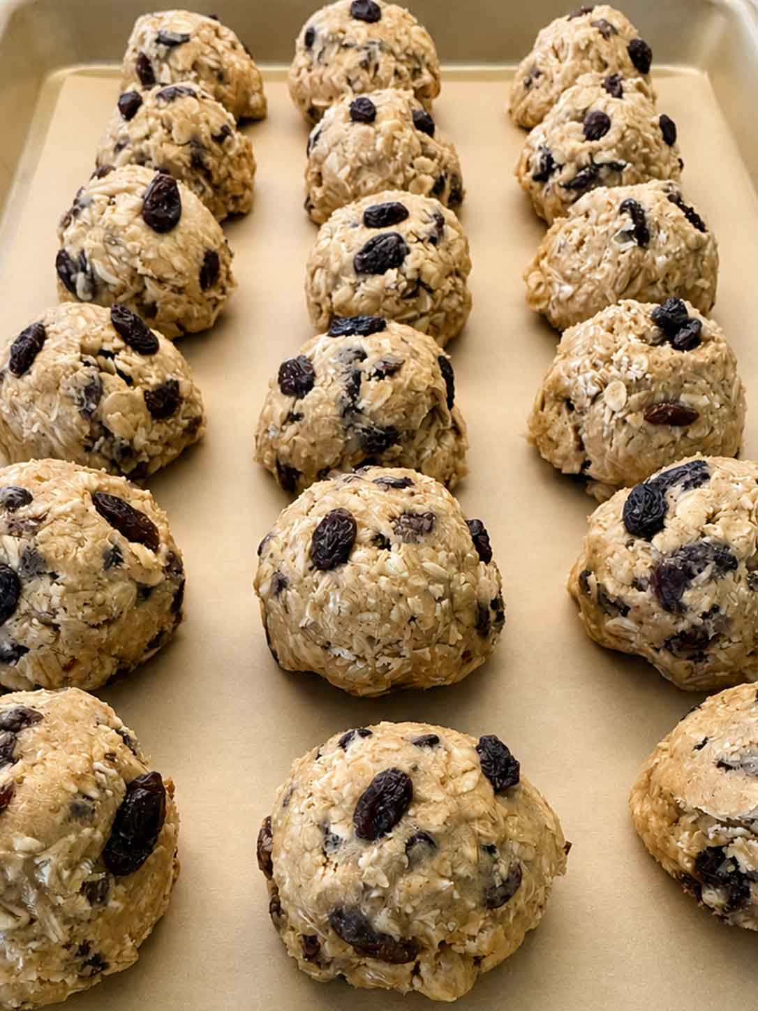 Rows of ready-to-bake sourdough oatmeal cookie dough balls on a parchment-lined tray.