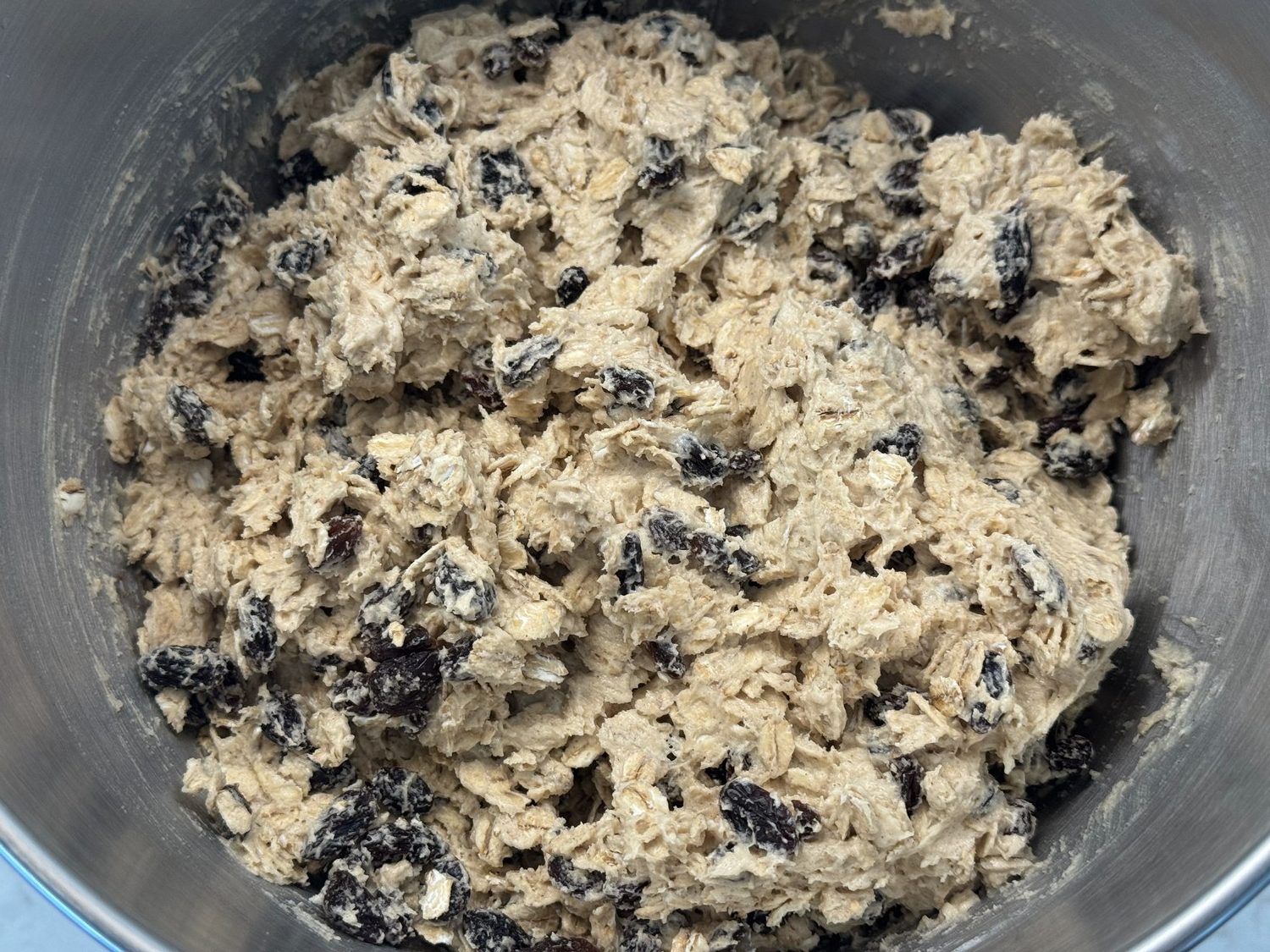 Finished sourdough oatmeal cookie dough in a mixing bowl, thick and studded with oats and raisins.