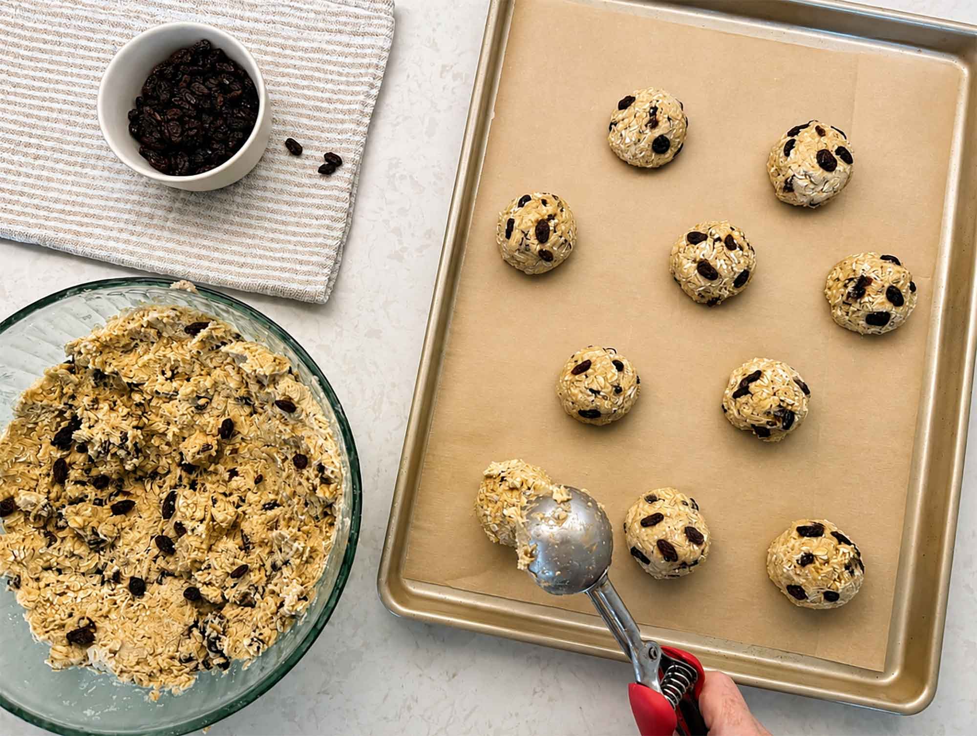 Overhead view of sourdough oatmeal cookie dough being scooped into mounds on a parchment-lined baking sheet.
