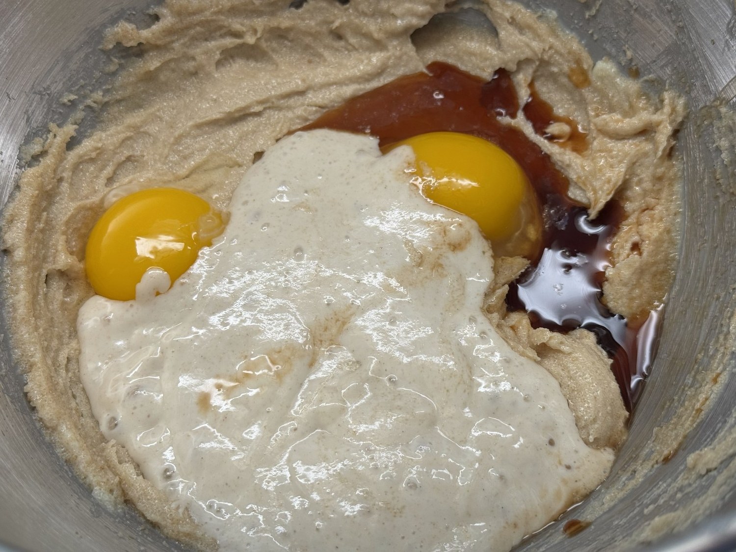 Egg, egg yolk, sourdough starter, and vanilla added on top of creamed butter and sugar in a mixing bowl.
