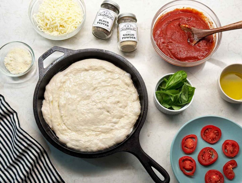 Toppins for sourdough pizza crust such as mozzarella cheese, parmesan cheese, pizza sauce, basil, and tomatoes