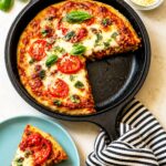 Sourdough Pizza Dough Recipe (Crispy + Chewy, Same Day!) Slice of sourdough pizza on a blue plate beside a cast-iron skillet with a deep dish pizza topped with mozzarella, tomatoes, and fresh basil