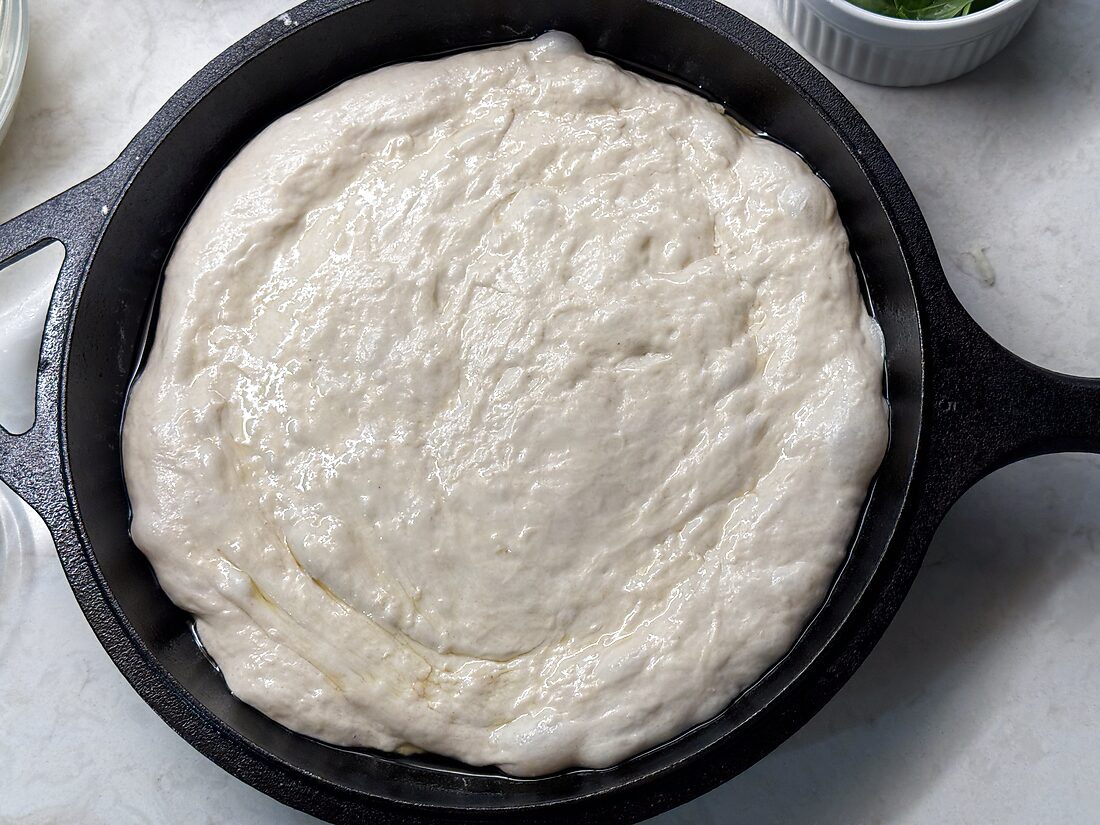 Sourdough pizza dough pressed into the bottom and up the sides of a 10-inch cast iron skillet for a deep dish crust
